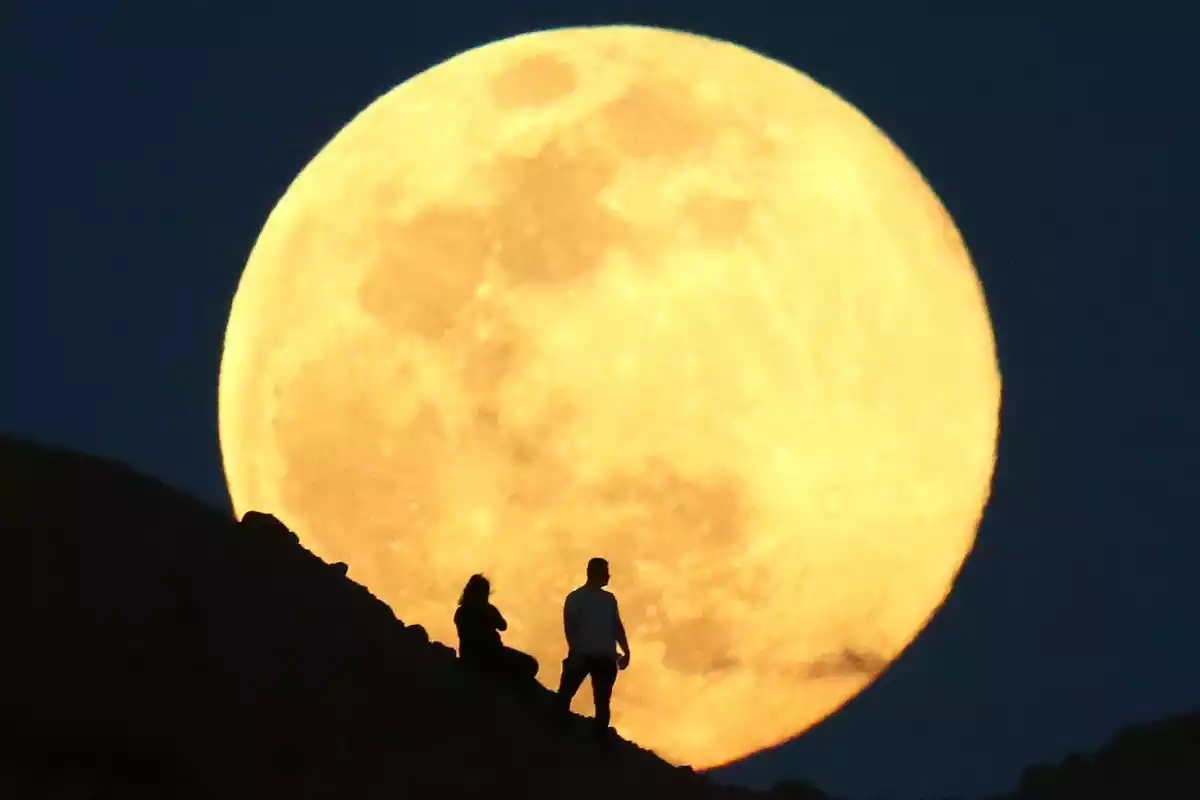 Imagen de dos personas observando una Luna llena