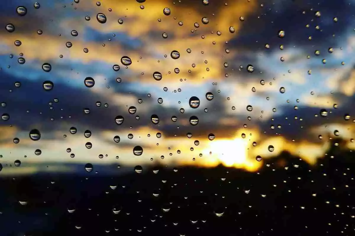 Imagen de un cristal con gotas de lluvia en una puesta de sol