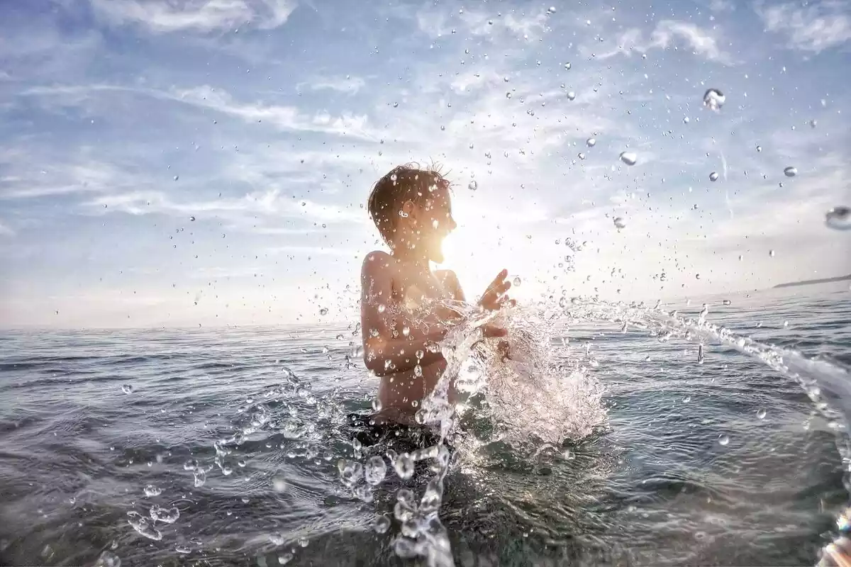 Niño salpicando agua dentro de la playa