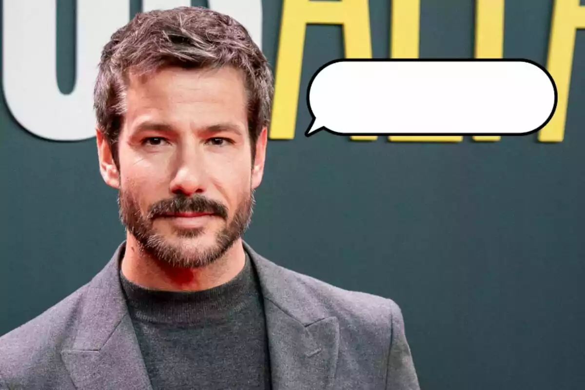 Un hombre con barba y cabello oscuro lleva un traje gris y está de pie frente a un fondo con letras amarillas. Hay un globo de diálogo vacío al lado de su cabeza.