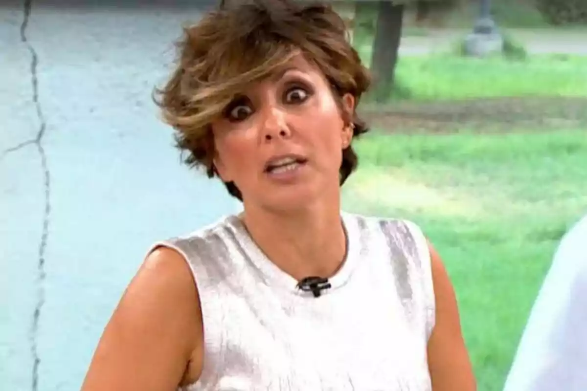 Una persona con expresión sorprendida y cabello corto, vestida con una blusa sin mangas, en un entorno al aire libre.