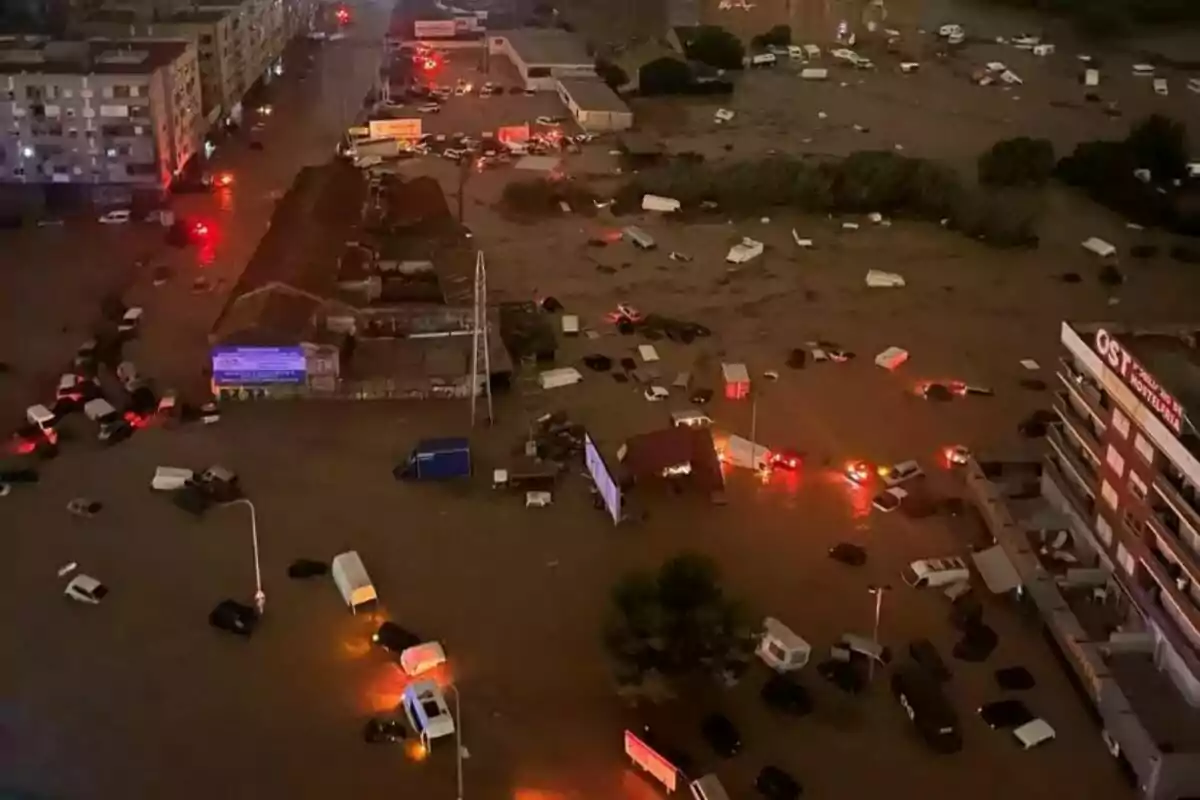 Vista aérea de una ciudad inundada durante la noche con vehículos sumergidos y luces de emergencia encendidas.