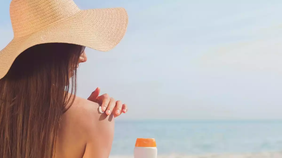 Una mujer pondiéndose crema solar en una playa